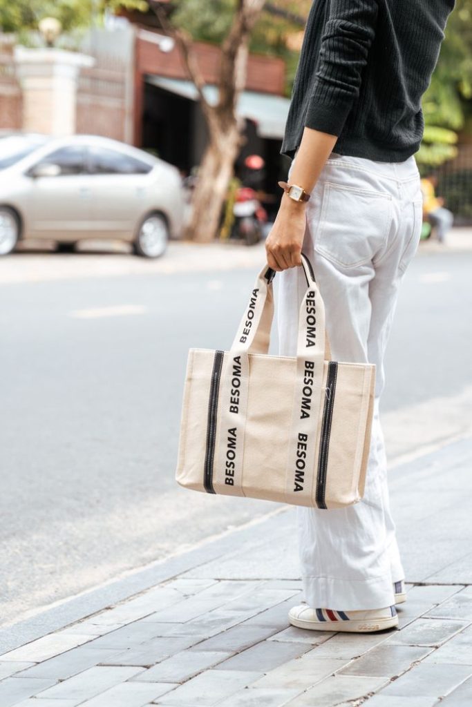 Stylish outdoor scene with woman holding a branded tote bag on the sidewalk.