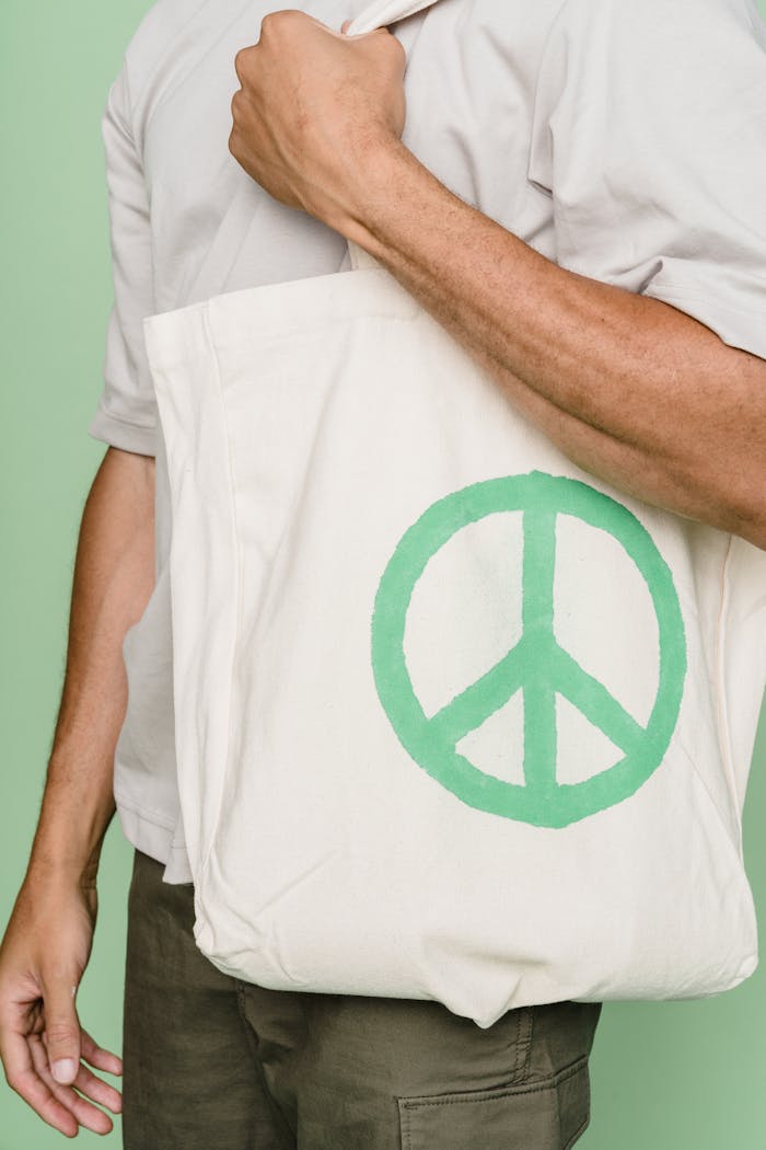 services-07 Close-up of a person carrying a tote bag with a green peace symbol, emphasizing sustainability.